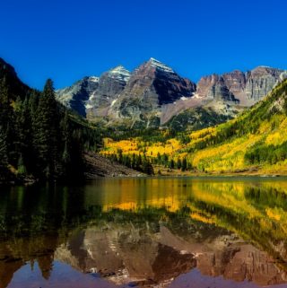 A close up of a hillside next to a body of water with Maroon Bells in the background