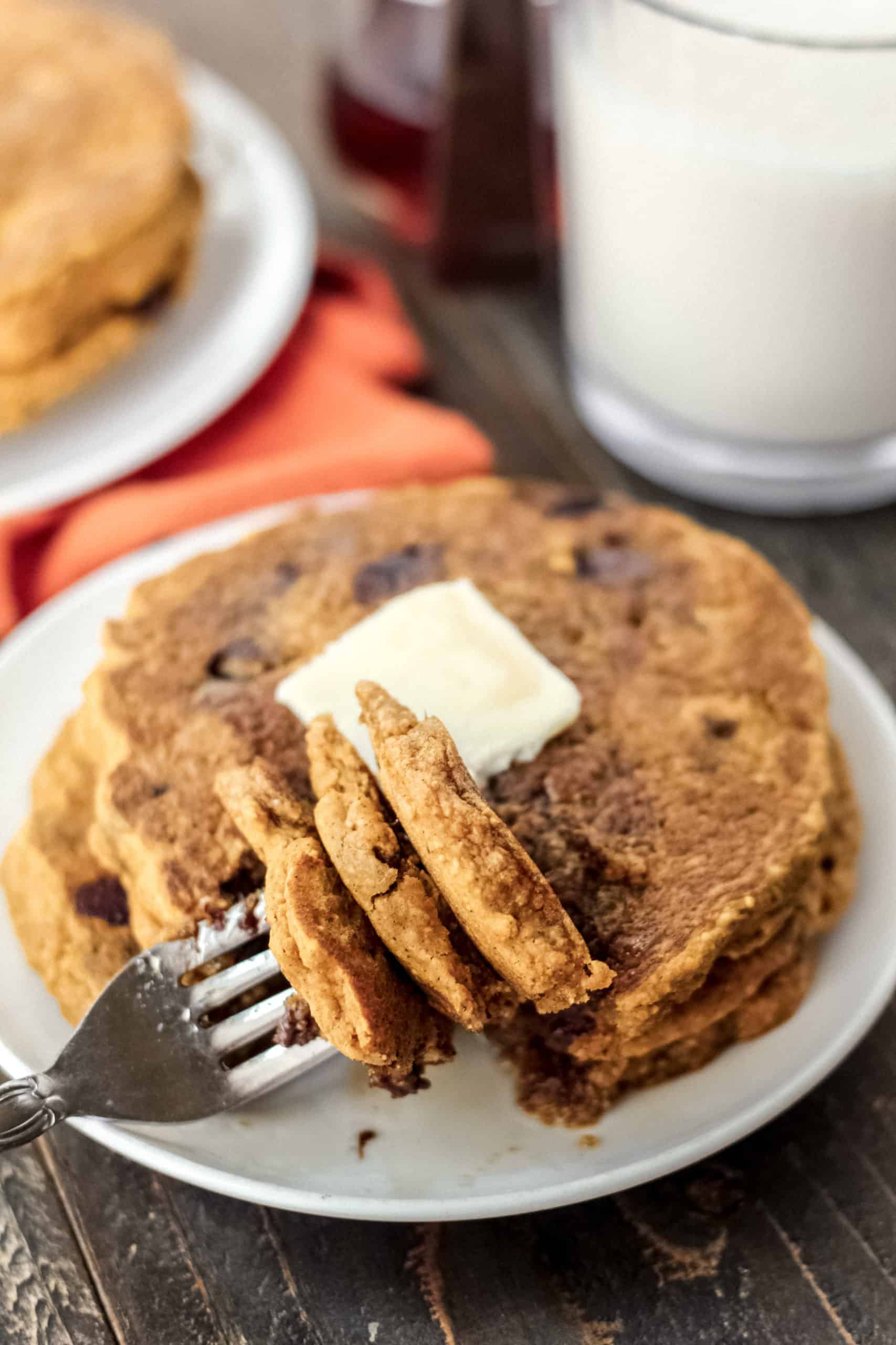 A stack of three pumpkin pancakes on a plate with a fork holding a bite