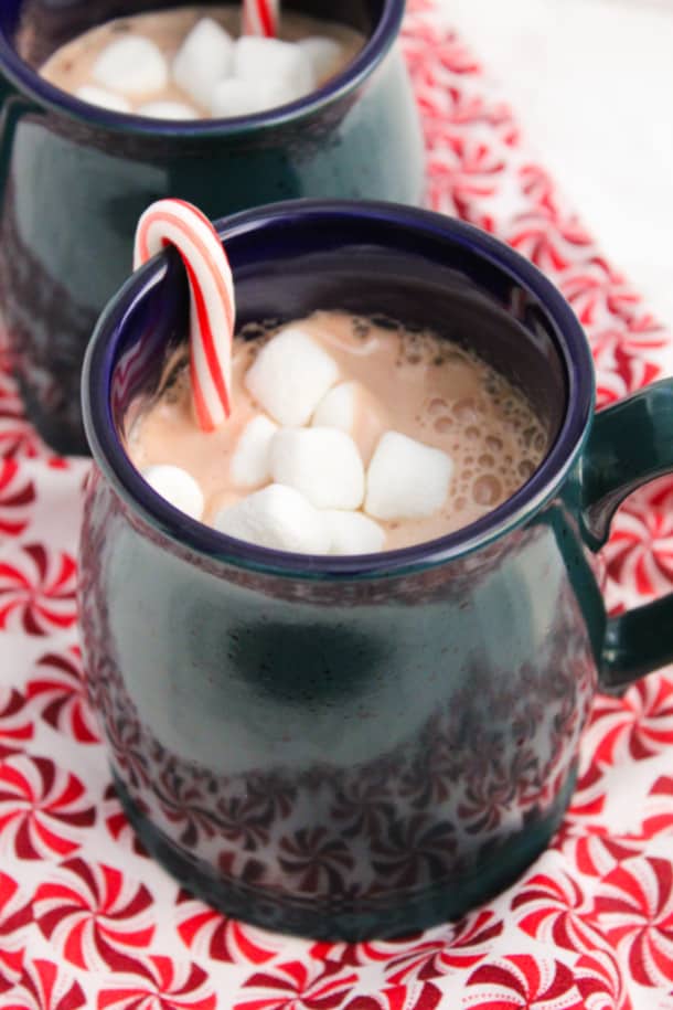 A mug of Peppermint Hot Cocoa with marshmallows and a mini candy cane sticking out
