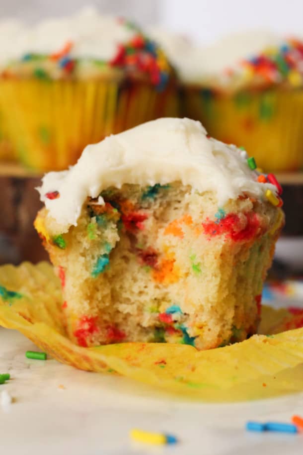 One close up Gluten-free Funfetti Cupcake with the cupcake liner peeled open and a bite taken out