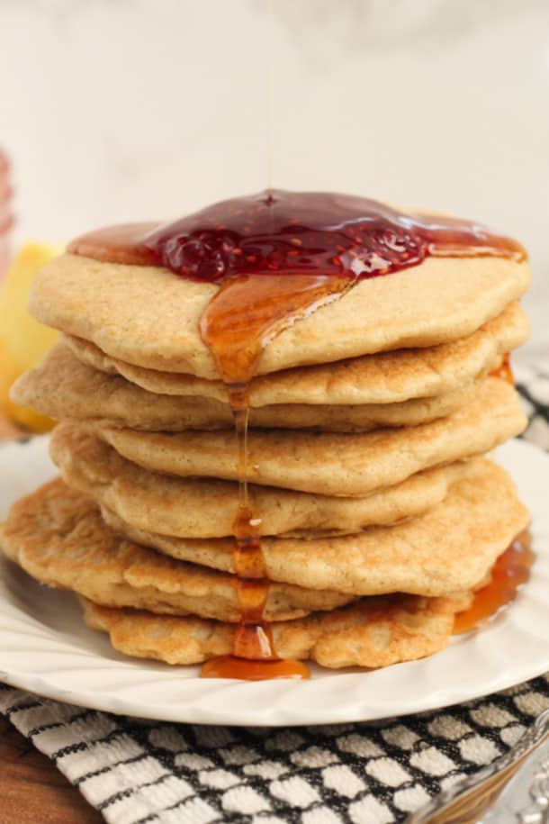 Stack of lemon pancakes viewed from the side, on a plate, with maple syrup dripping down the side
