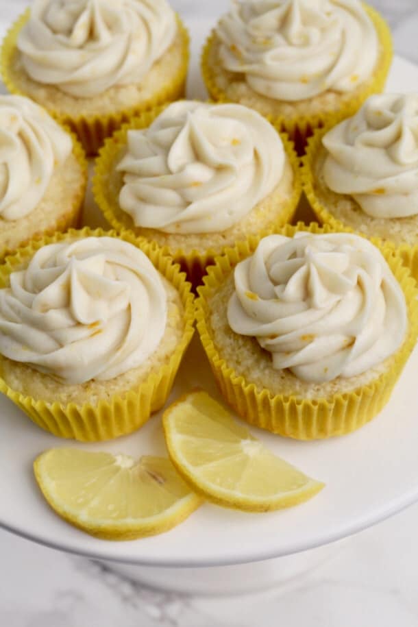 Lemon Cupcakes on a cake tray with yellow cupcake liners, with slices of lemons