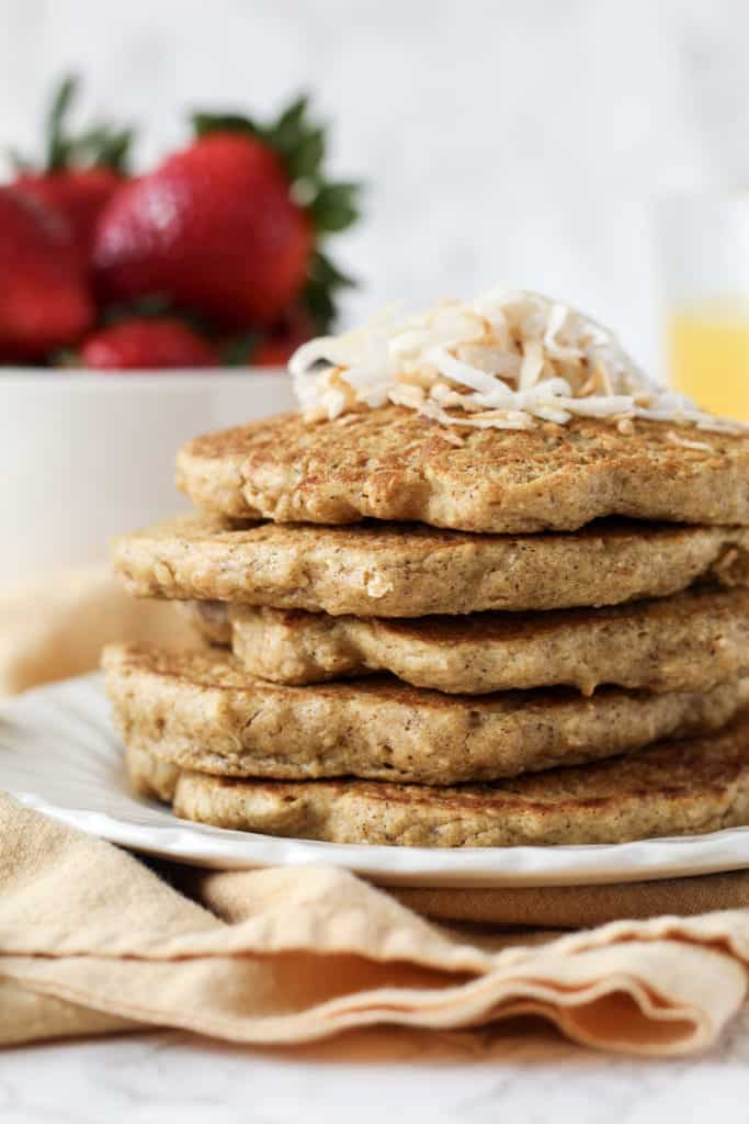 side view of a stack of Toasted Coconut Oat Pancakes on a plate