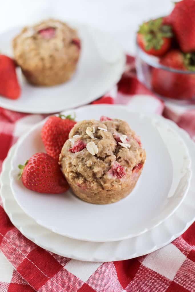 Double Strawberry Oat Muffin on two plates with two strawberries from a top down view