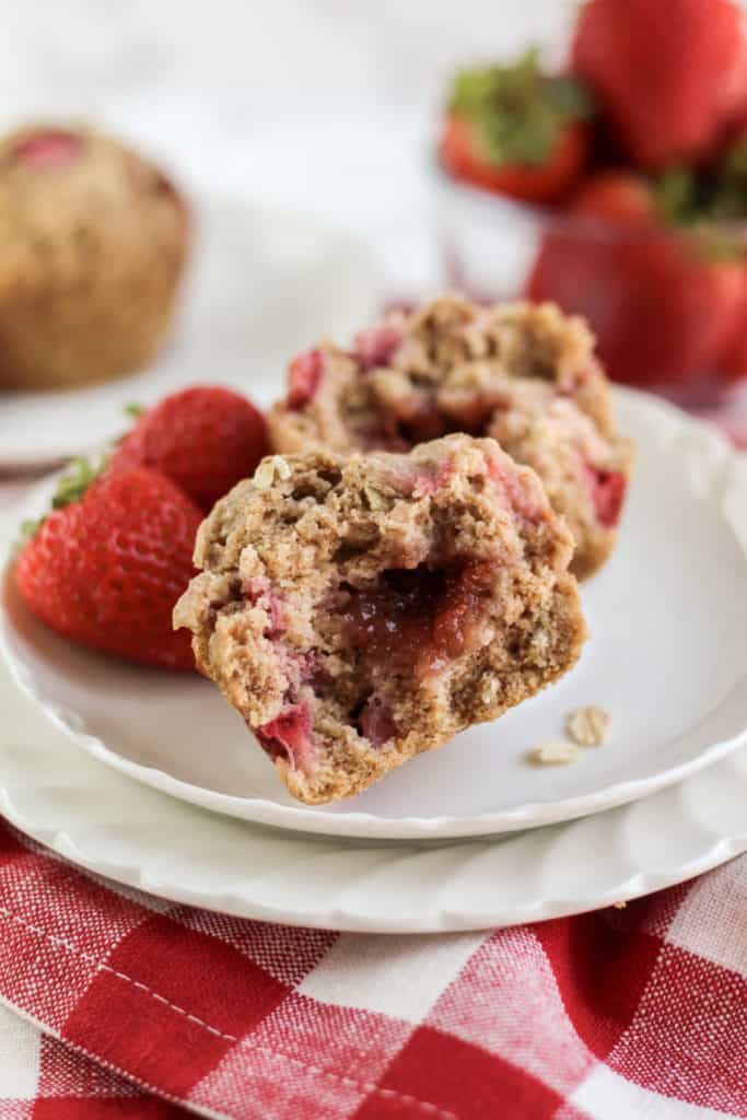 Double Strawberry Oat Muffin cut in half on two plates with two strawberries