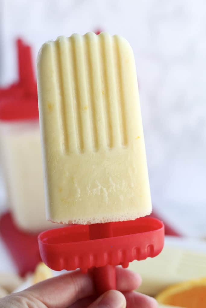 one Orange Creamsicle Popsicles held up by a hand