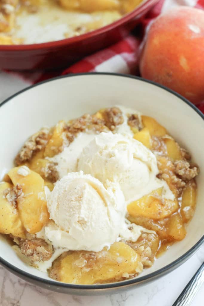 A bowl with healthy peach crisp and two scoops of vanilla ice cream on top