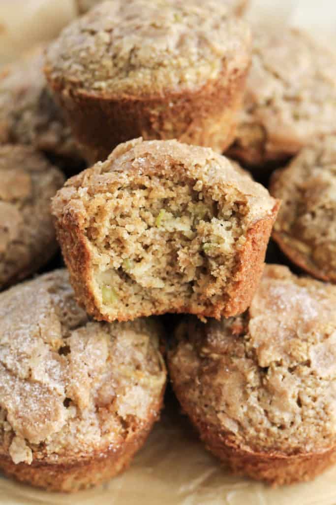 A stack of Apple Cinnamon Oat Muffins with one on top with a bite taken out of it
