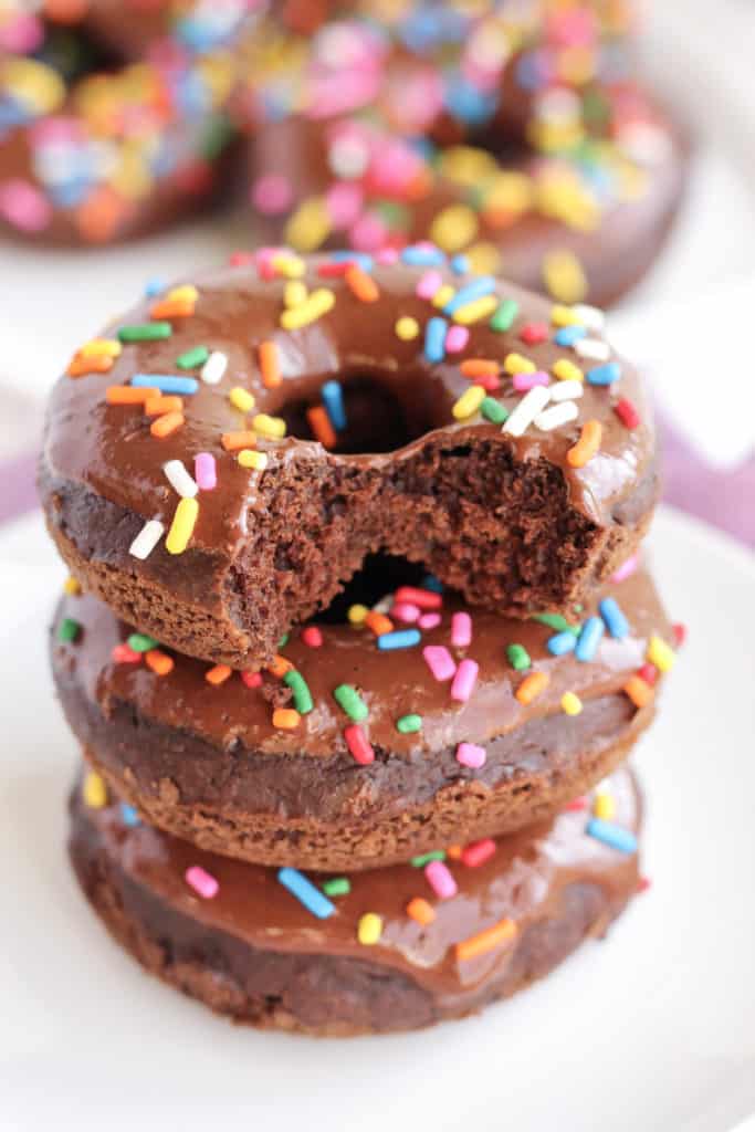 A stack of three Chocolate Donuts with a bite taken out of the top of one