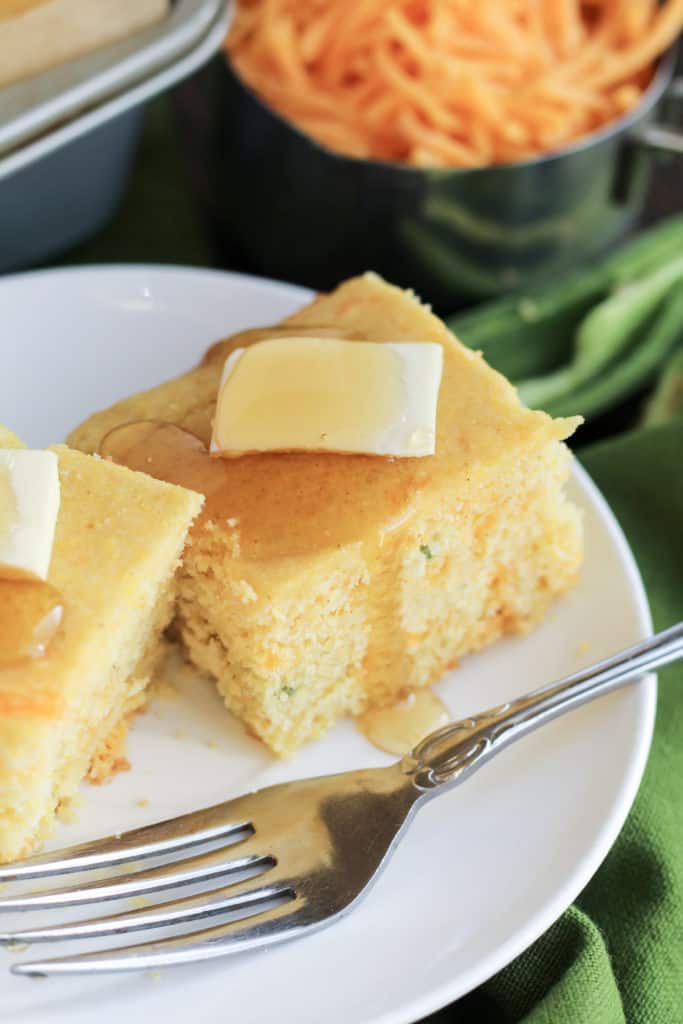 A plate with a close up view of Cheddar Jalapeno Cornbread with butter and honey on top, and a fork