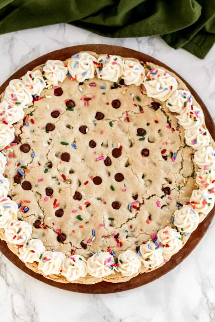 A cookie pizza on a pizza pan, with frosting around the edges.