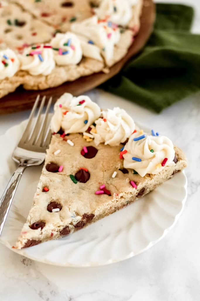 A piece of cookie pizza on a plate with a fork, with frosting and sprinkles.
