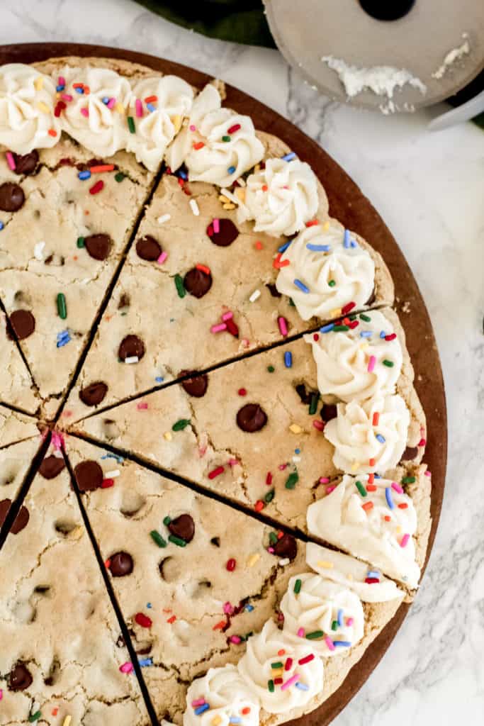 A close up of a cookie pizza with frosting on the edges, sliced in pieces.