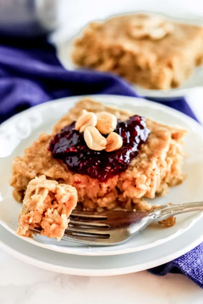 piece of peanut butter baked oatmeal with jelly and peanuts on top with a fork with a bite of oatmeal on it