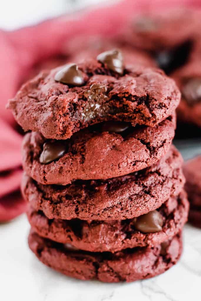 stack of Red Velvet Chocolate Chip Cookies with a bite taken out of the top one