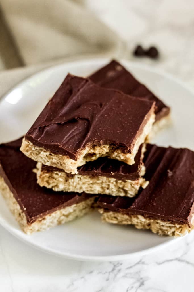 Plate with five no back Chocolate Peanut Butter Bars stacked, with a bite taken out of the top one