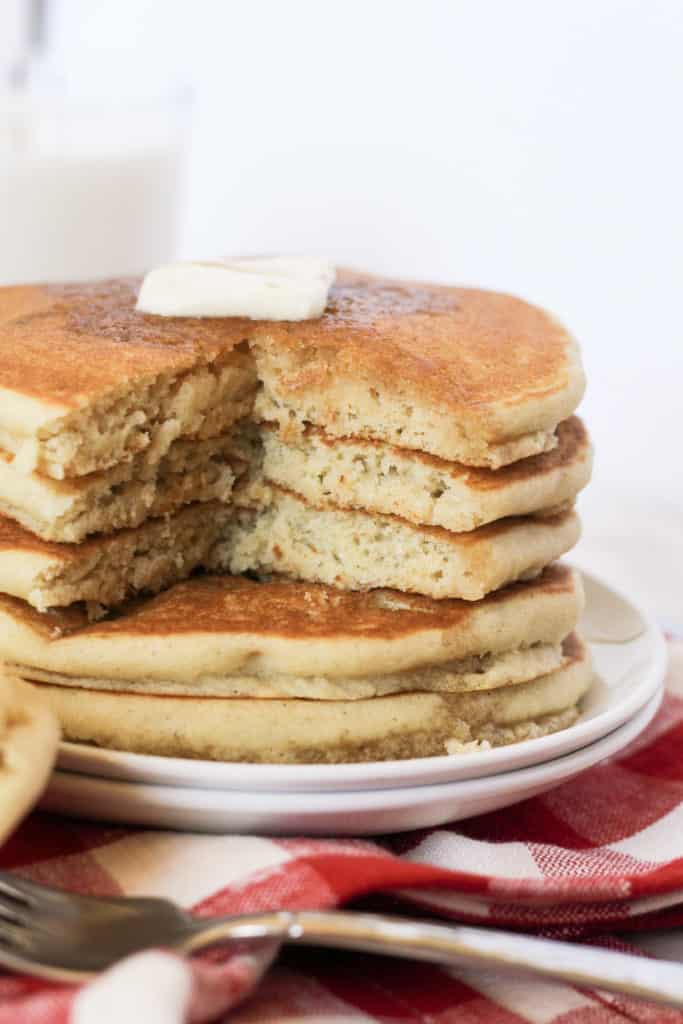Stack of three pancakes on a plate with a bite cut out.