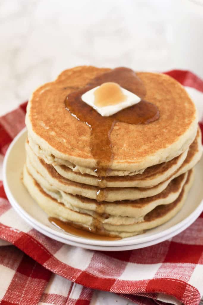 Stack of pancakes on a plate with butter and maple syrup.