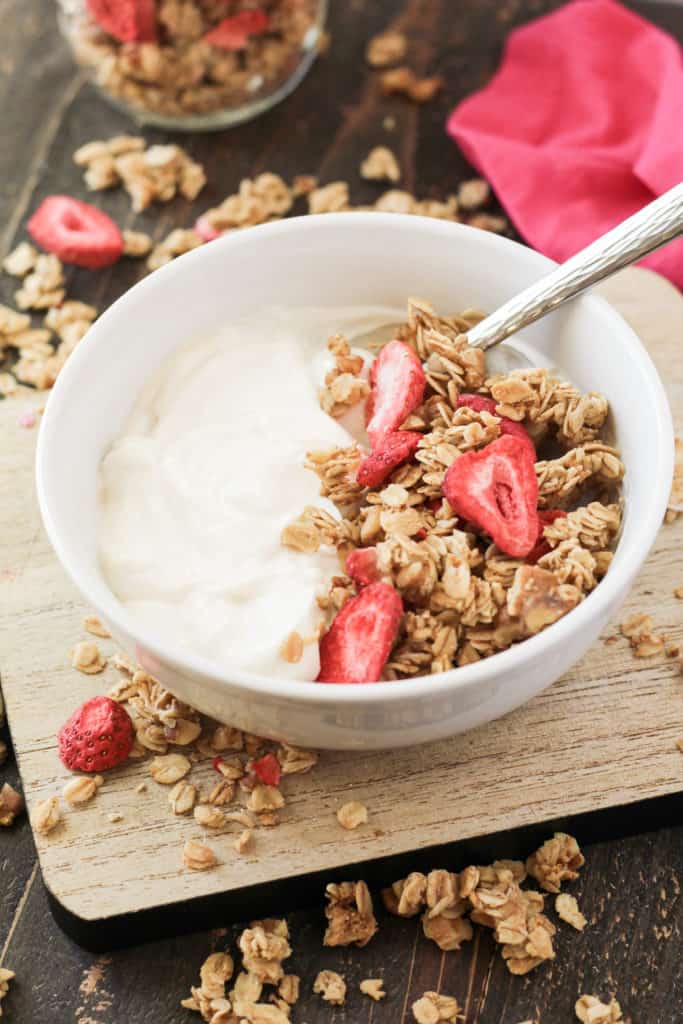 Bowl of yogurt with granola on top and a spoon.