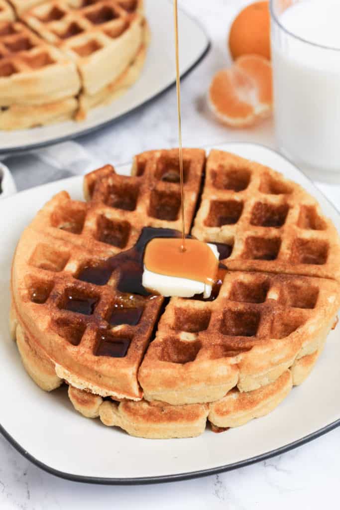 Plate of double stacked waffles with butter on top and maple syrup being poured on.