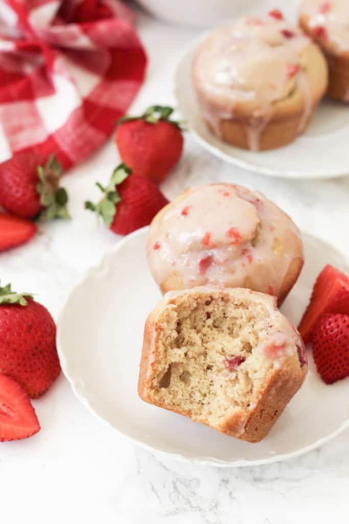 Two strawberry muffins on a plate with a bite taken out of one.