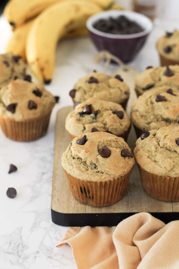 Muffins on a wood board, with chocolate chips and banana's around.