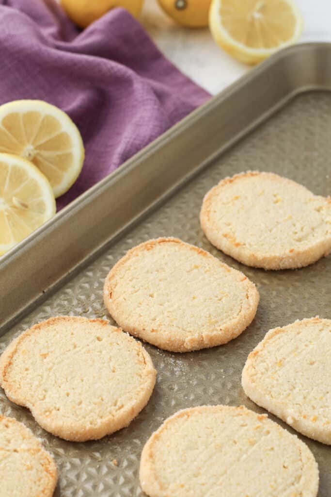 Cookies on a baking sheet with lemons and a purple dishcloth. 