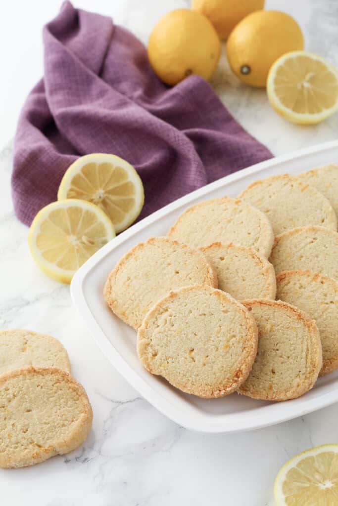 Cookies on a tray with lemons and a purple dishcloth behind.