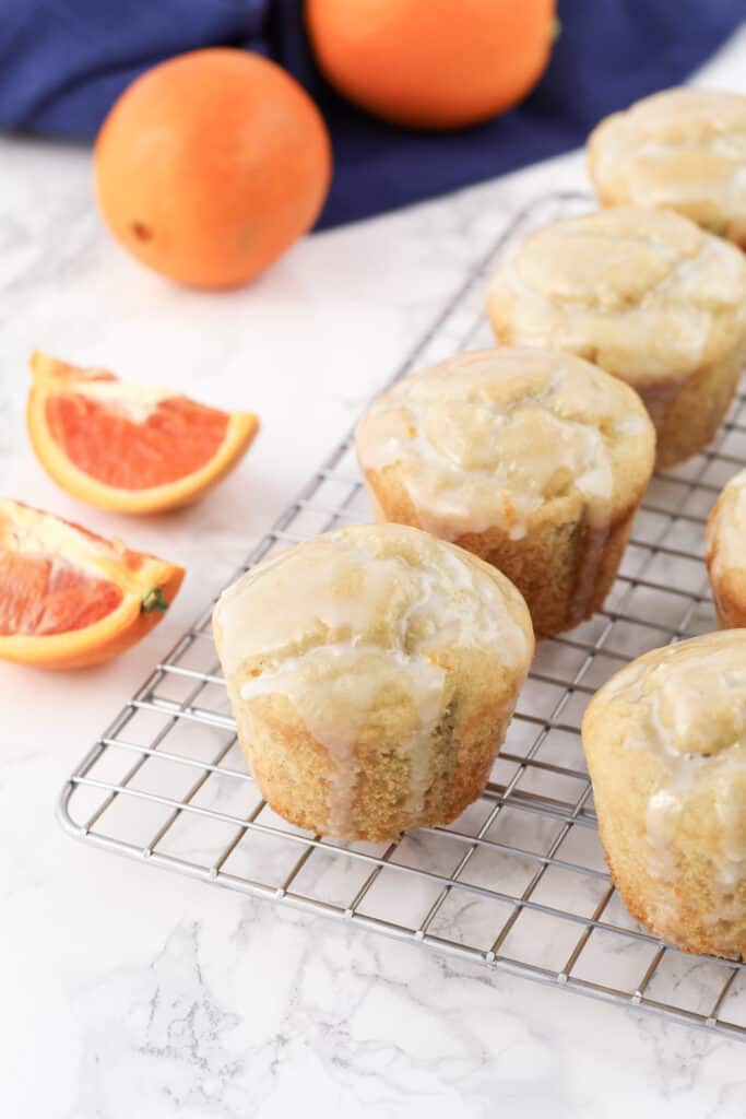 Muffins on a cooling rack with oranges in the background.