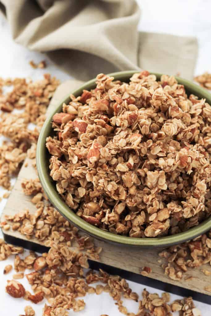 A bowl of granola on top of a tray with granola scattered around.